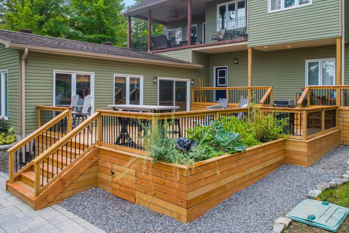 New cedar deck with stairs, black balusters and a built-in planter box behind a green vinyl-sided house