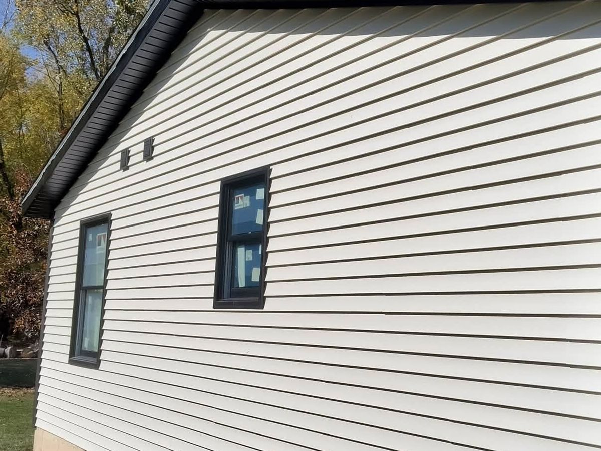 Cream horizontal vinyl siding on a gable wall with two new black-framed windows still in film